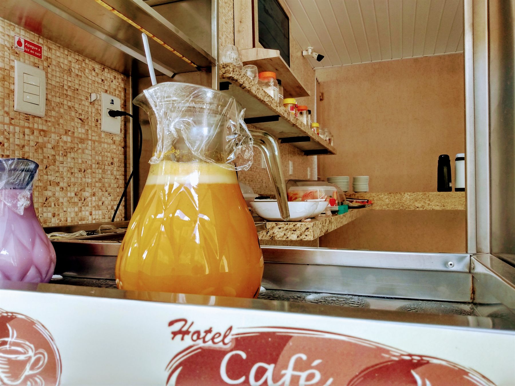 Balcão do café da manhã da pousada, com jarra de suco, garrafas térmicas, frutas e louças