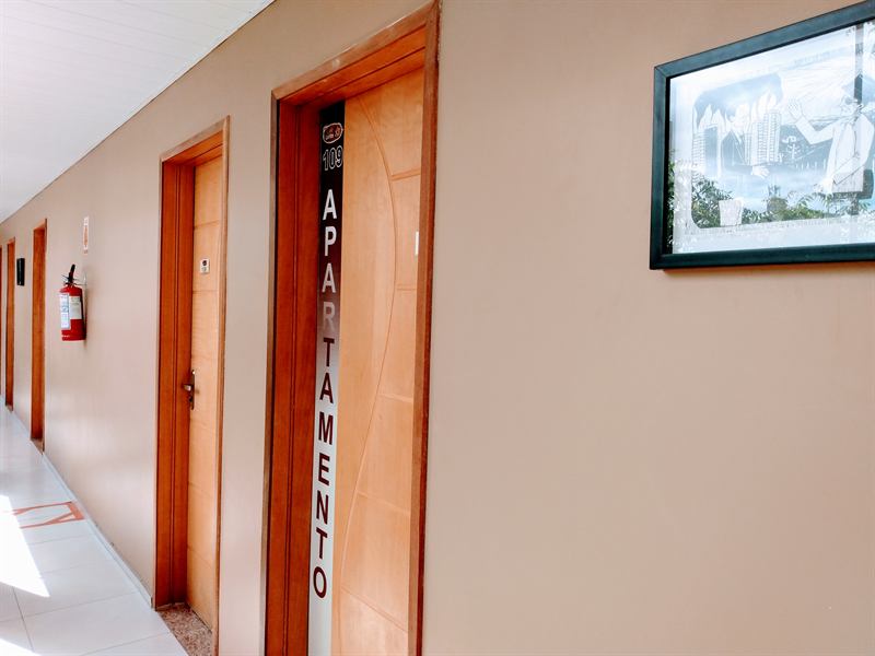 Corredor com portas de madeira dos apartamentos, placa vertical de numeração e extintor de incêndio