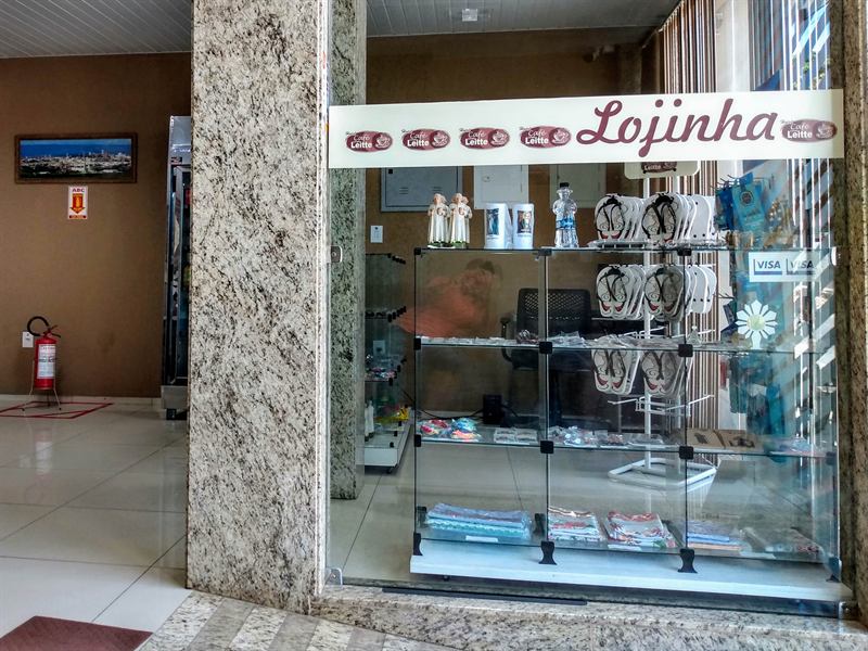 Entrada da lojinha da pousada, com letreiro e vitrine de vidro exibindo sandálias e lembranças
