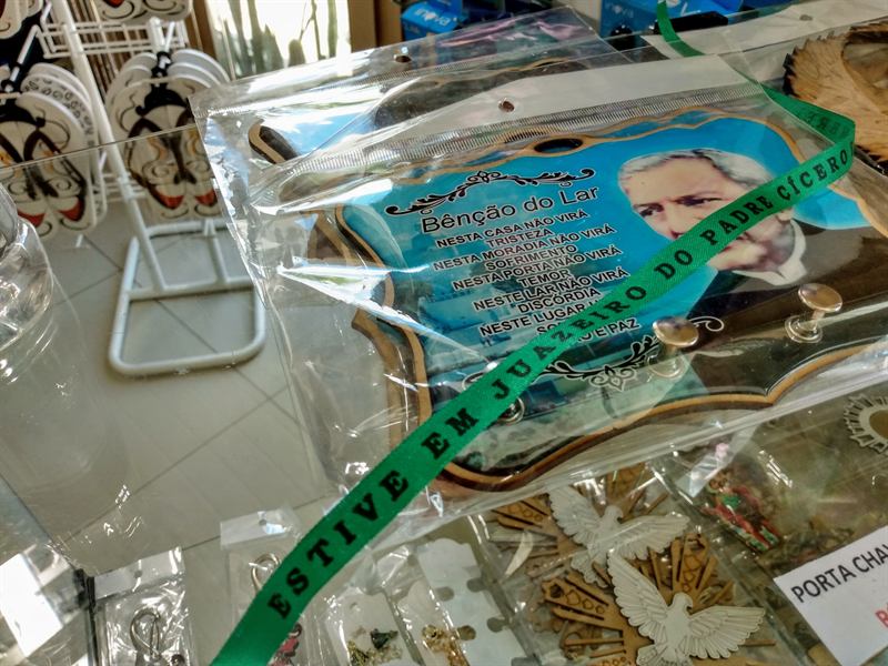 Quadro Bênção do Lar e fita de recordação de Juazeiro do Padre Cícero sobre a vitrine de vidro