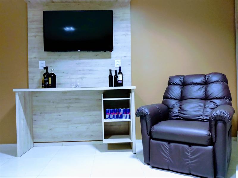 Ambiente de estar do apartamento com TV na parede amadeirada, bancada de bebidas e poltrona reclinável marrom