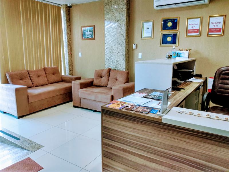 Recepção com balcão de atendimento em madeira, sofás marrons e certificados de avaliação na parede