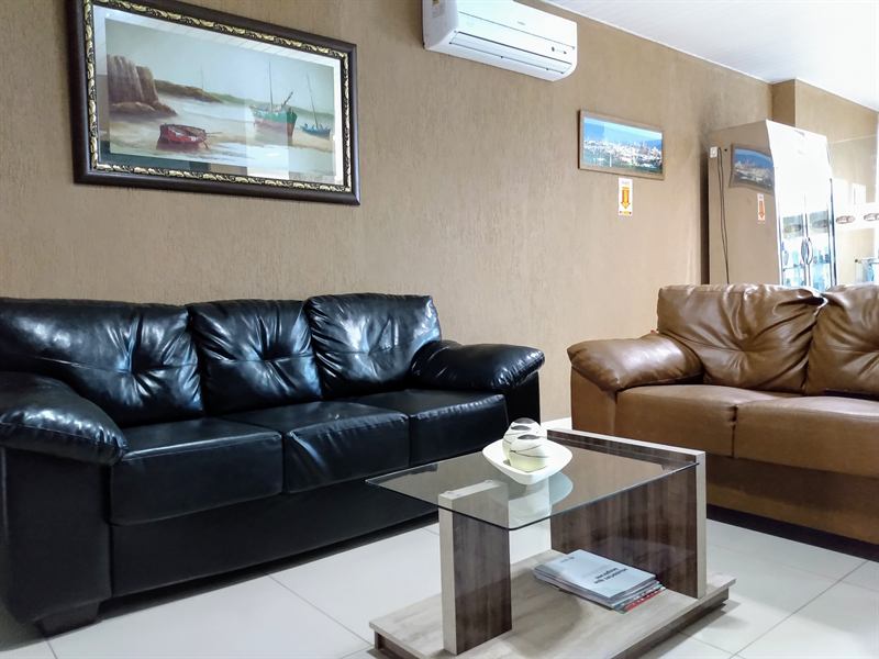 Sala de espera com sofás de couro preto e marrom, mesa de centro de vidro e quadro de barcos na parede