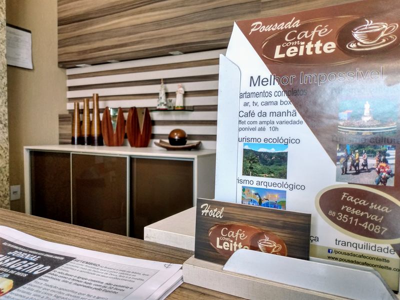Material informativo da pousada sobre o balcão, com destaque para o telefone de reservas e a decoração em madeira