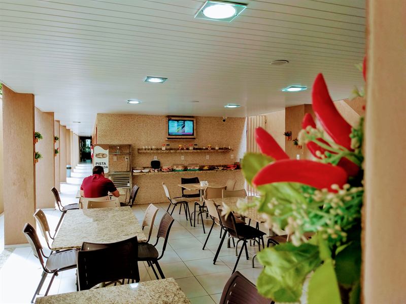 Hóspede sentado tomando o café da manhã no salão do refeitório, com o buffet ao fundo
